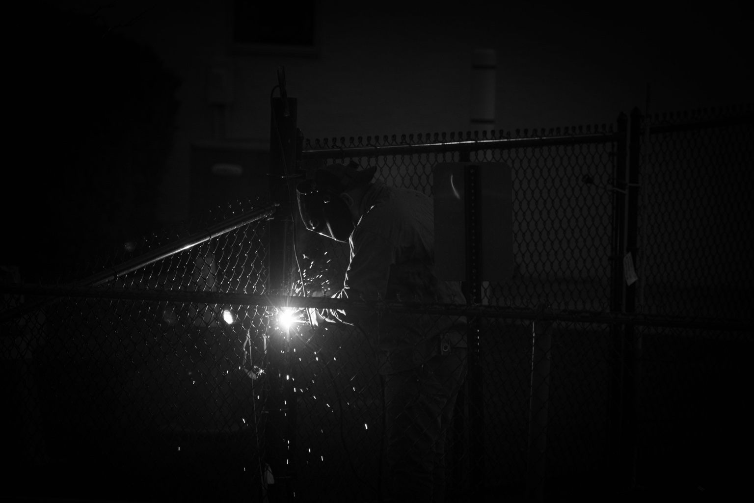 Welder working on a metal fence with sparks visible